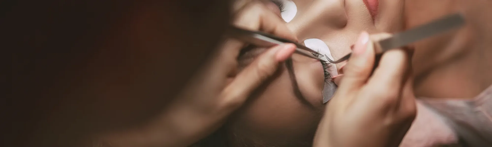 A lash artist placing an individual extension with tweezers